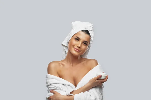 Woman in bathrobe holding cream jar. — Stock Photo, Image