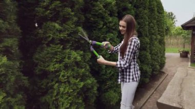 Mutlu kız dekoratif thuja 'nın aşırı gelişmiş dallarını kesiyor.