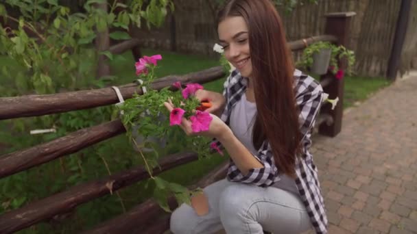 Beautiful young girl taking off dry leaves from flower pot — Stock Video