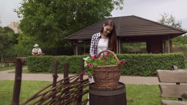 Mladá dívka výsadba květiny, zatímco starší muž řezání keře — Stock video