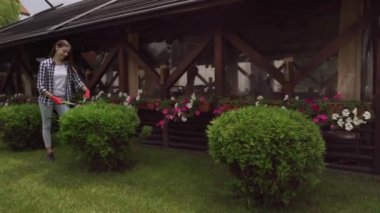 Gülümseyen genç bayan çim biçme makinesiyle çalıları kesiyor.