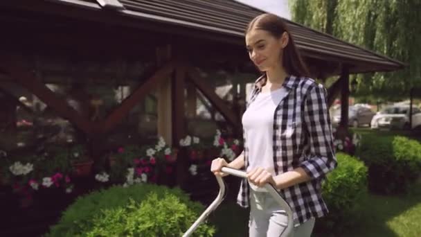 Красивая девушка стрижет траву газонокосилкой в солнечный день — стоковое видео