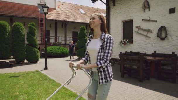 Senhora encantadora com cabelo castanho cortar grama com movedor de grama — Vídeo de Stock