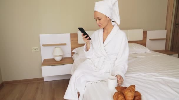 Chica usando el teléfono, bebiendo café en la cama . — Vídeos de Stock