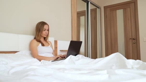 Mujer escribiendo en el ordenador portátil en la cama . — Vídeos de Stock