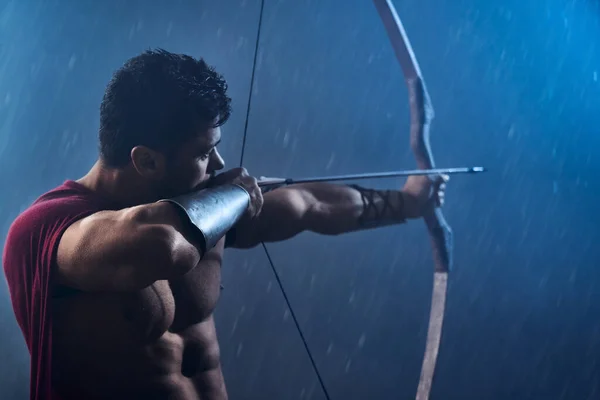 Muskulöser Spartaner in rotem Mantel schießt aus Bogen. — Stockfoto