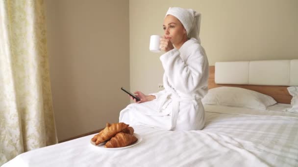 Vrouw die telefoon gebruikt, koffie drinkt op bed. — Stockvideo