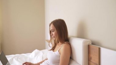 Yatakta dizüstü bilgisayar kullanan genç bir kadın.