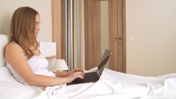 Жінка друкує на ноутбуці в ліжку . — стокове відео