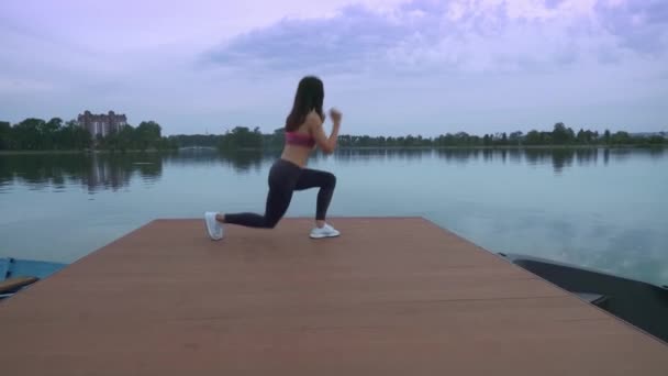 Fitness žena dělá výpady na jezeře molo. — Stock video