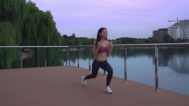 Mujer de fitness haciendo saltos en el muelle del lago . — Vídeos de Stock