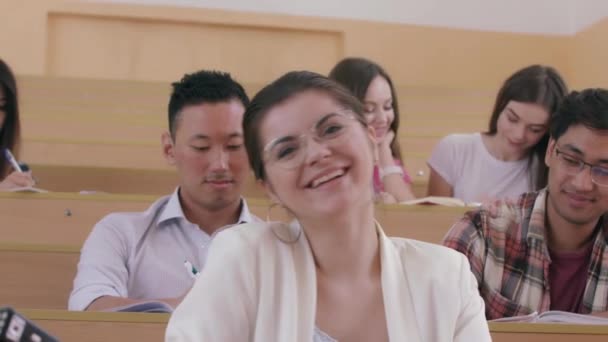 Lächelndes Mädchen schreibt in Werbebuch im Hörsaal der Universität. — Stockvideo