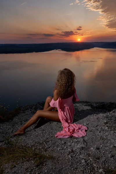 Sexy dziewczyna siedzi i podziwiając zachód słońca w pobliżu jeziora. — Zdjęcie stockowe