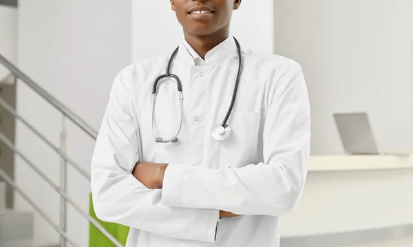 Médecin africain souriant en manteau avec les bras croisés . — Photo