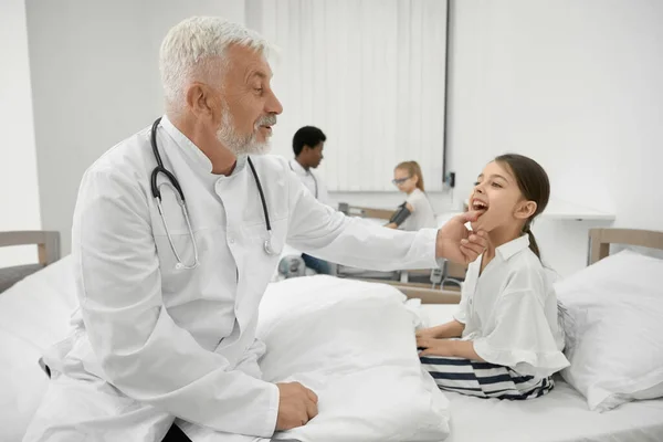 Medico anziano che esamina la gola della studentessa sul divano . — Foto Stock