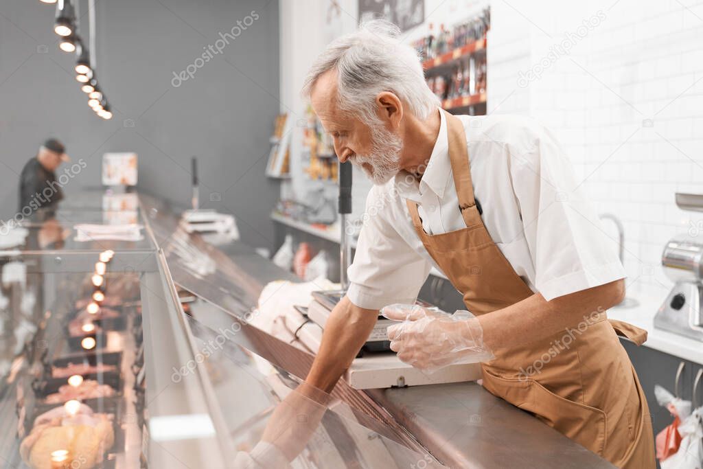 Male butcher taking raw meat out of counter.