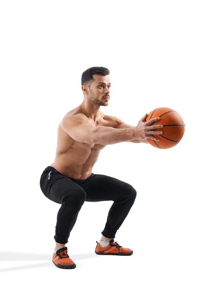 Sportman doet squats terwijl hij basketbal vasthoudt. — Stockfoto