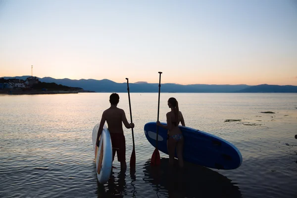 Silueta de hermosa pareja con surfear y remar en el océano. Concepto estilo de vida, deporte, amor — Foto de Stock