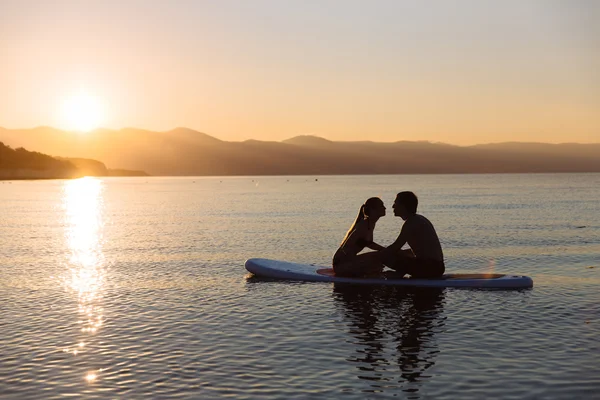 Silueta de hombre y chica sexy joven besándose en sup surf en el océano bajo el sol. Concepto estilo de vida, deporte, amor — Foto de Stock