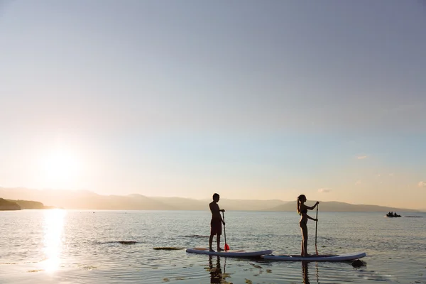 Silhouette von männlichen und weiblichen auf sup surf schwimmen im Ozean. Konzept Lifestyle, Sport, Liebe — Stockfoto