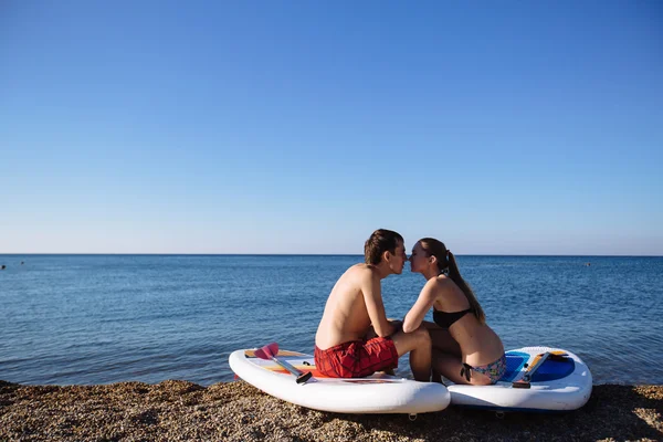 Hombre y joven sexy chica besándose en sup surf en el océano bajo el sol. Concepto estilo de vida, deporte, amor — Foto de Stock