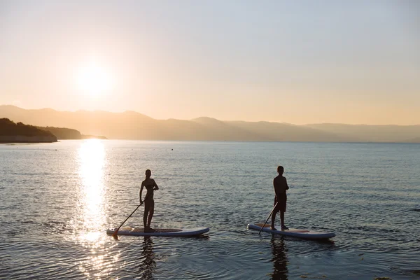 Silhouette von männlichen und weiblichen auf sup surf schwimmen im Ozean. Konzept Lifestyle, Sport, Liebe — Stockfoto