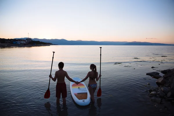 Silueta de macho, hembra con sup surf y remo en el océano. Concepto estilo de vida, deporte, amor — Foto de Stock