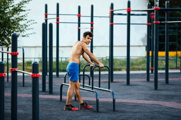 Muscular man warming up before exercise at crossfit ground doing push ups as part of training. Sport concept