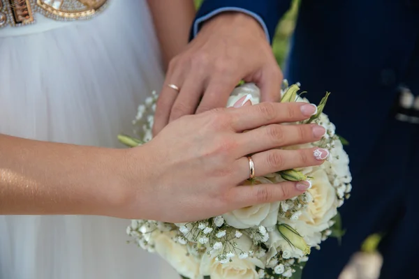 Bruden och brudgummar händer med vigselringar på bukett blommor — Stockfoto