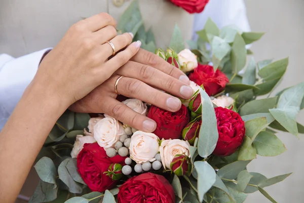 Bruden och brudgummar händer med vigselringar på bukett blommor — Stockfoto