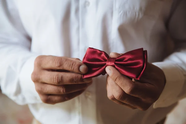 Esküvői kiegészítők. Vőlegény piros csokornyakkendő tartja a kezében — Stock Fotó