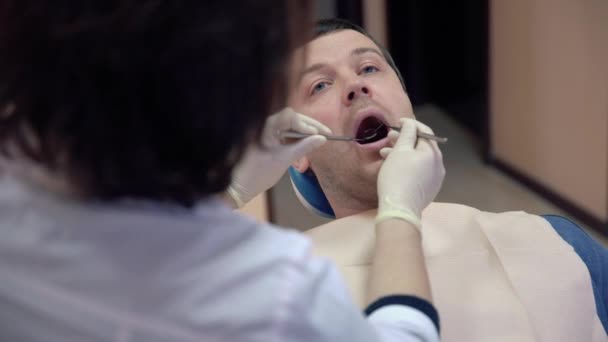 Женщина дантист делает процедуры для пациента мужского пола в клинике, закрыть — стоковое видео