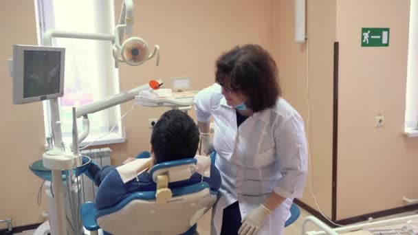 Kadın dişçi klinikte prosedürleri önce erkek hasta ile konuşmak — Stok video