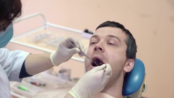 Женщина дантист делает процедуры для пациента мужского пола в стоматологическом кабинете, закрыть. Концепция здоровья — стоковое видео