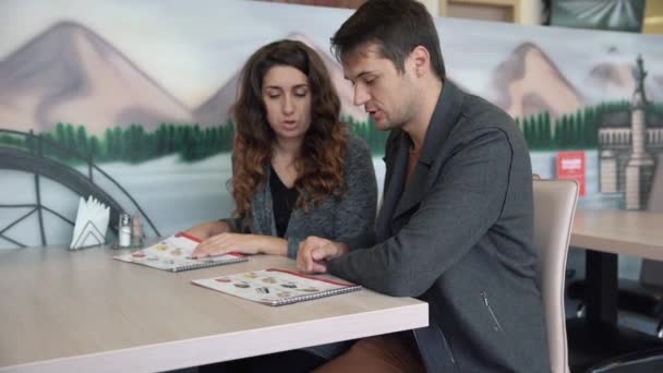 Ένα νεαρό ζευγάρι σε μια ρύθμιση εστιατόριο βλέπουν ένα μενού. — Αρχείο Βίντεο