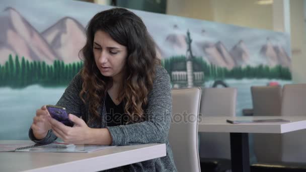 Hermosa joven sentada en una mesa en un café, hablando por teléfono — Vídeo de stock