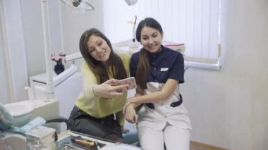 iki güzel kız dişçi ve hasta selfie gülümseme ve reklam diş Kliniği ile smartphone üzerinde yordamlar sonra yapıyor. Mutlu müşteri. Sağlıklı yaşam kavramı