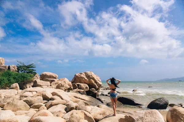 Сексуальна дівчина в шортах і купальник, що стоїть на тлі морської трави, що піднімається. красивий краєвид з великими каменями — стокове фото