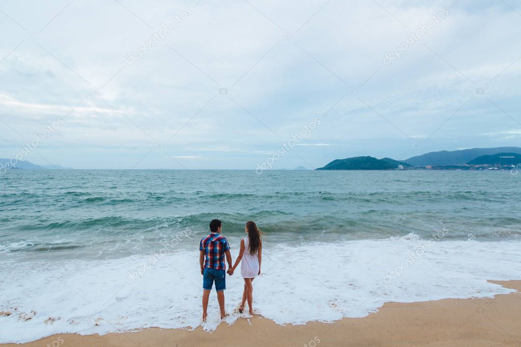 Just married couple hold each others hands, turned back stand and look at the sea