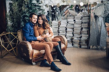 Kollarını sarılma, gülümseyen ve öpüşme koltukta oturan bir kedi ile güzel çift aşık. Aile kavramı