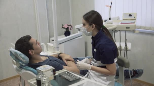 Jong meisje tandarts maken van procedures met tanden mannelijke patiënt. Arts behandelt tanden. Concept oh gezond leven — Stockvideo