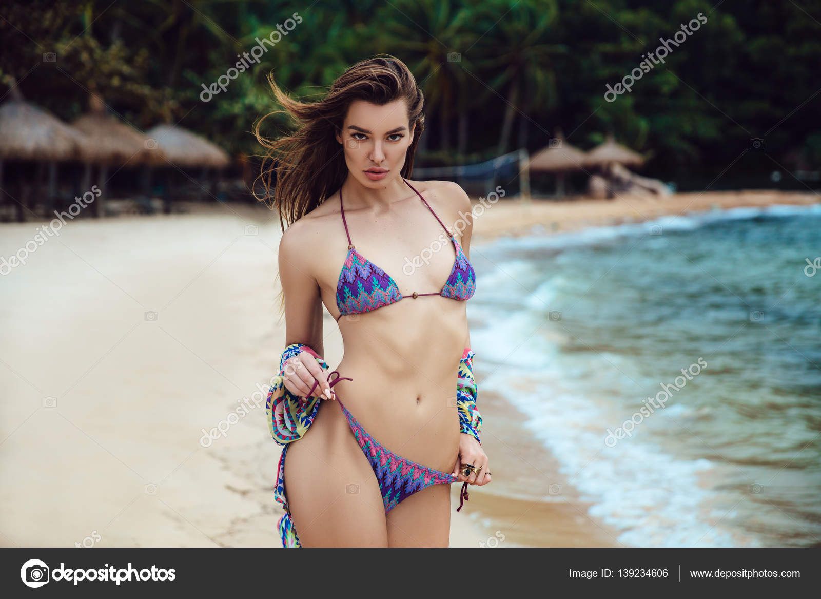 Beautiful young brunette woman in blue bikini posing on the beach