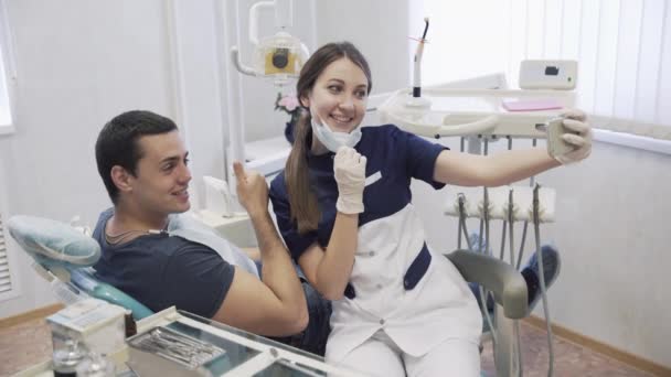 Gyönyörű lány fogorvos és férfi beteg csinál selfie mosollyal és fogászati klinikán laught smartphone eljárások után. Boldog ügyfél. Az egészséges élet fogalma — Stock videók