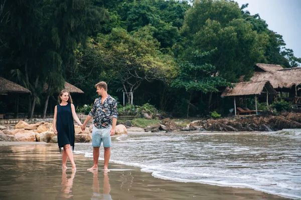 Belo jovem casal apaixonado segurando as mãos e andando na praia, olhando para o mar. paisagem. Conceito de lua de mel — Fotografia de Stock