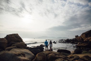 Siluet genç bir çift deniz plaj yaz aylarında döndü elele aşık. Mavi gömlek ve beyaz elbiseli kız saçında bir çelenk ile adam. Balayı konsepti