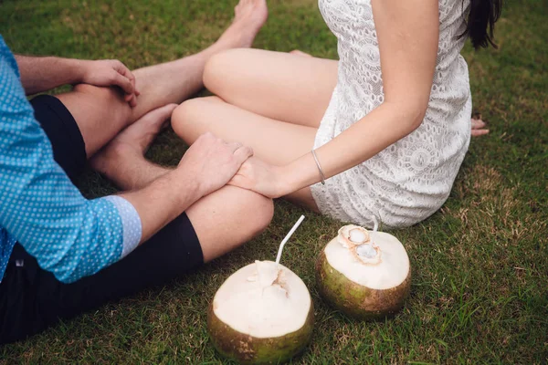 Mooie paar met kokosnoten houden hun handen op de golfbaan in zomer close-up. man dragen het blauwe shirt en het meisje in een witte jurk. Concept van wittebroodsweken — Stockfoto