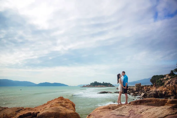 Młoda para w miłości, przytulanie i trzymając się za ręce na plaży Morza latem. Człowiek w niebieskiej koszulce i dziewczyna w białej sukni z wieniec w jej włosy — Zdjęcie stockowe