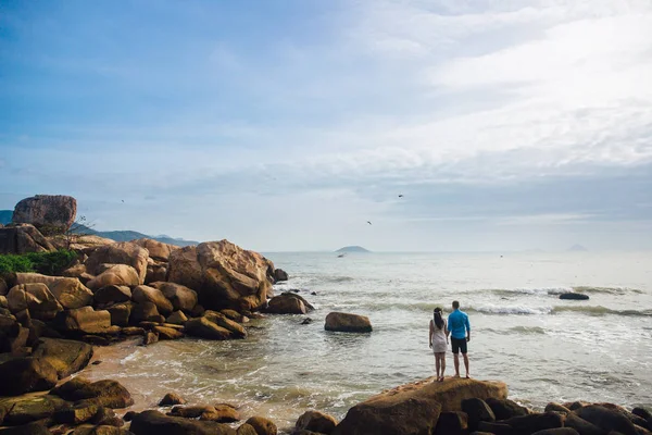 Young couple in love holding hands, turned back at sea beach in summer. The man in the blue shirt and the girl in a white dress with a wreath in her hair. Concept of honeymoon — Stock Photo, Image