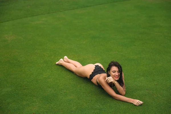 Young sexy and beautiful brunette fitness girl in black swimsuit posing turning booty shows ass at the green grass of Golf club. Sexy model portrait with perfect body. Concept of summer holiday — Stock Photo, Image