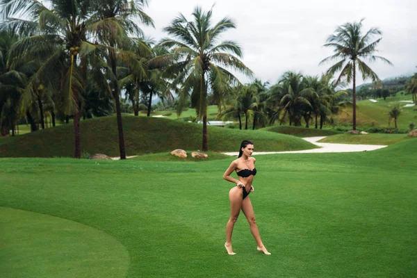 ポーズを回転戦利品黒の水着で若い綺麗でセクシーなブルネットのフィットネス女の子はゴルフ クラブの緑の芝生の上でお尻を示しています。完璧なボディのセクシーなモデルの肖像画。夏の休日の概念 — ストック写真